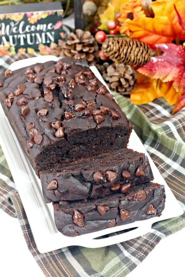 sliced loaf of double chocolate pumpkin bread on a white serving platter, with fall decor in the background