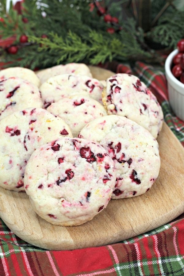 cranberry orange shortbread cookies displayed on a wooden cutting board, with Christmas greenery in the background
