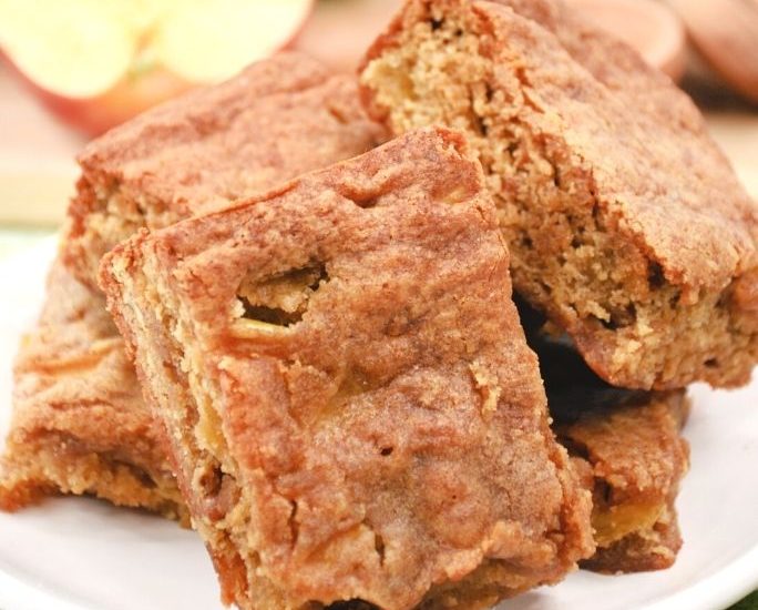 apple blondies on a white plate, with a sliced apple in the background