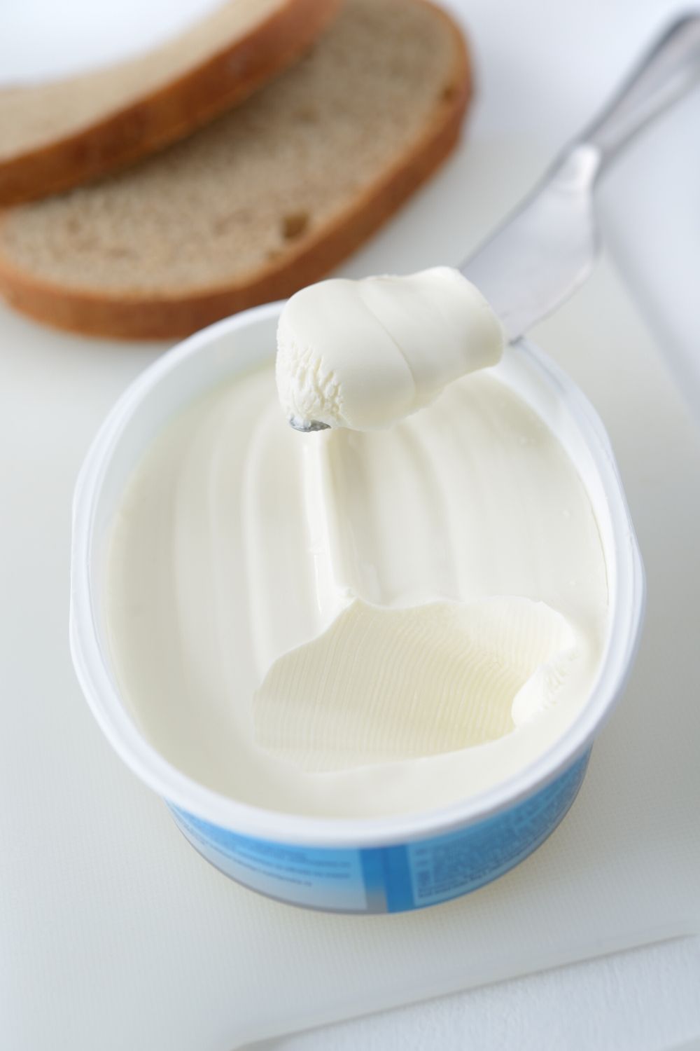 cream cheese in a container, with some scooped out on a knife.