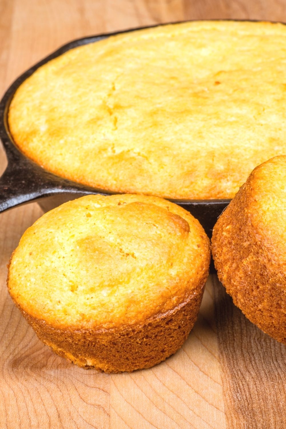 cast iron skillet of cornbread with two cornbread muffins in front of it