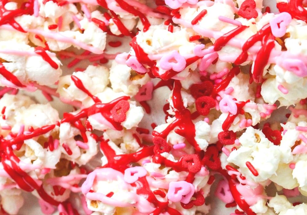 popcorn coated in white chocolate, drizzled with red and pink melted candy, then sprinkled with valentines sprinkles.