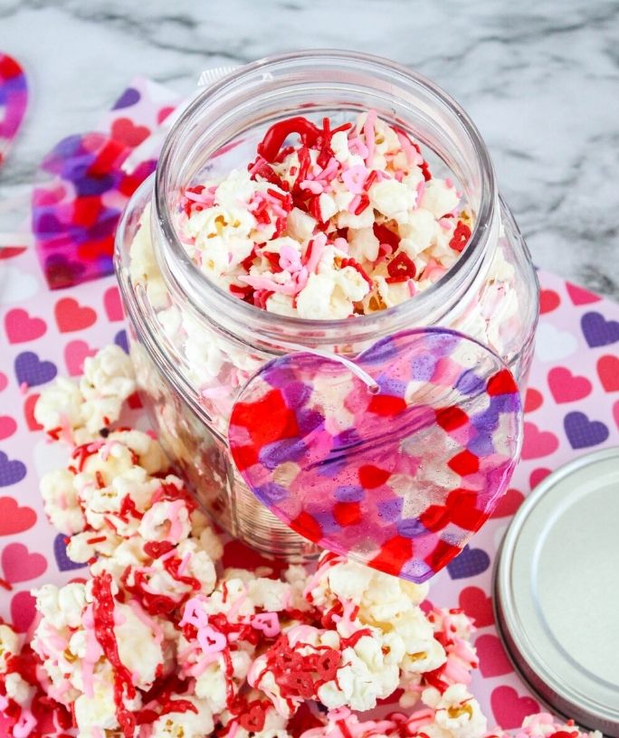 valentines day sweetheart popcorn in a jar, with more popcorn scattered around it