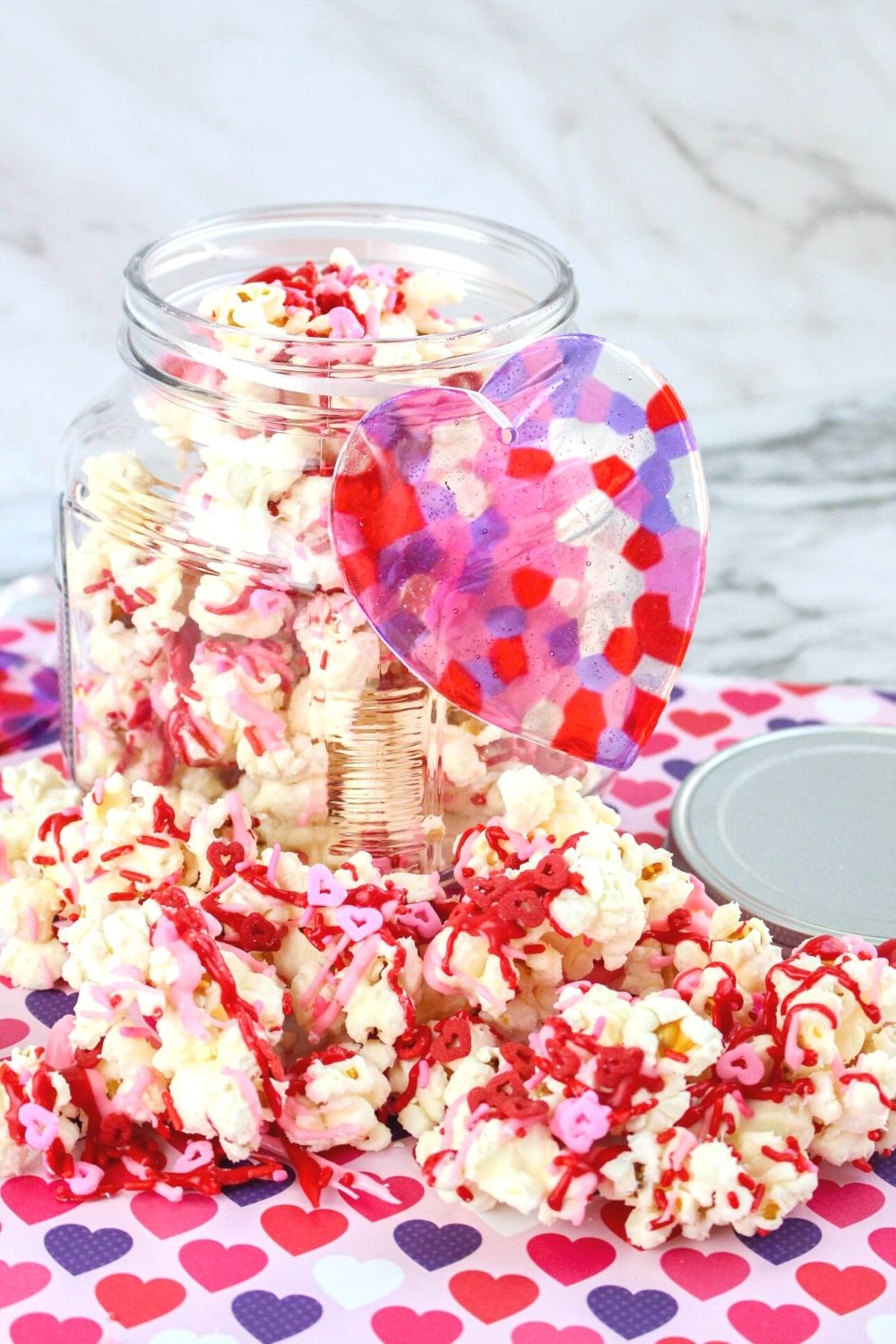 valentines day popcorn in front of a glass jar filled with more popcorn, resting on a decorative heart background