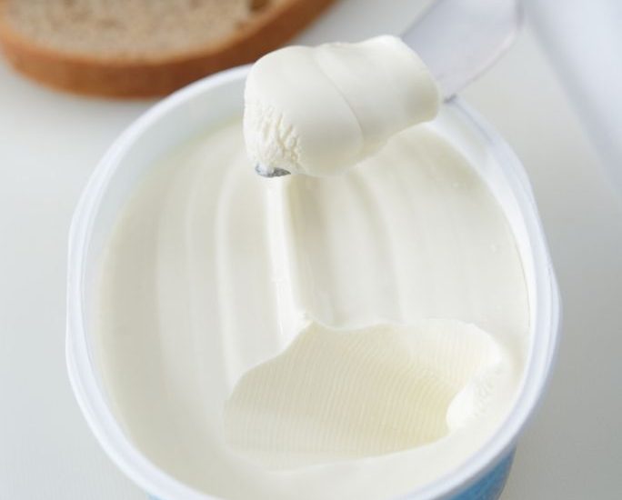 a plastic tub of cream cheese with a knife scooping some out. Whole grain bread is in the background