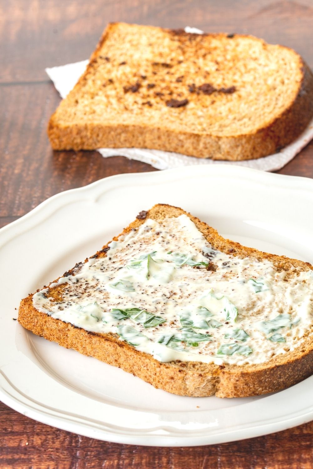 mayonnaise and chopped fresh basil spread on a piece of toast on a white plate