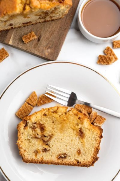 overhead view of a slice of stroopwafel cake served on a white plate, with coffee and the remaining cake in the background