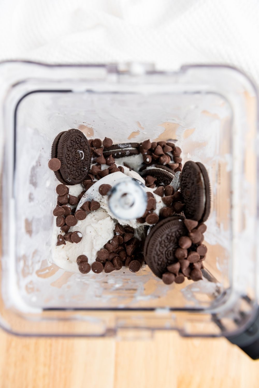 overhead view of the jar of a blender filled with ice, milk, cream, powdered sugar, vanilla extract, chocolate chips, and Oreo cookies.