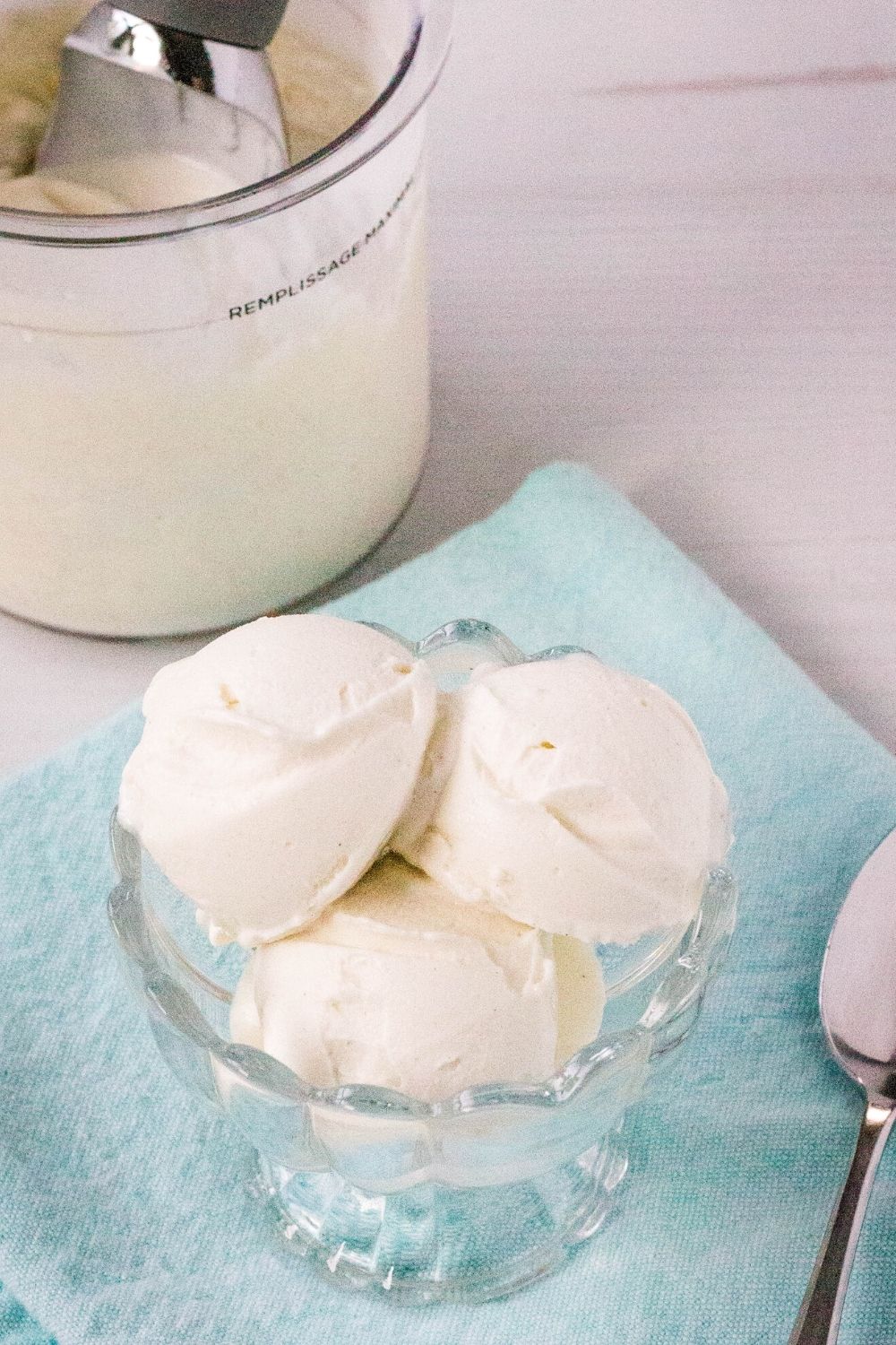 3 scoops of vanilla frozen yogurt in a glass dish, with the ninja creami pint of frozen yogurt in the background