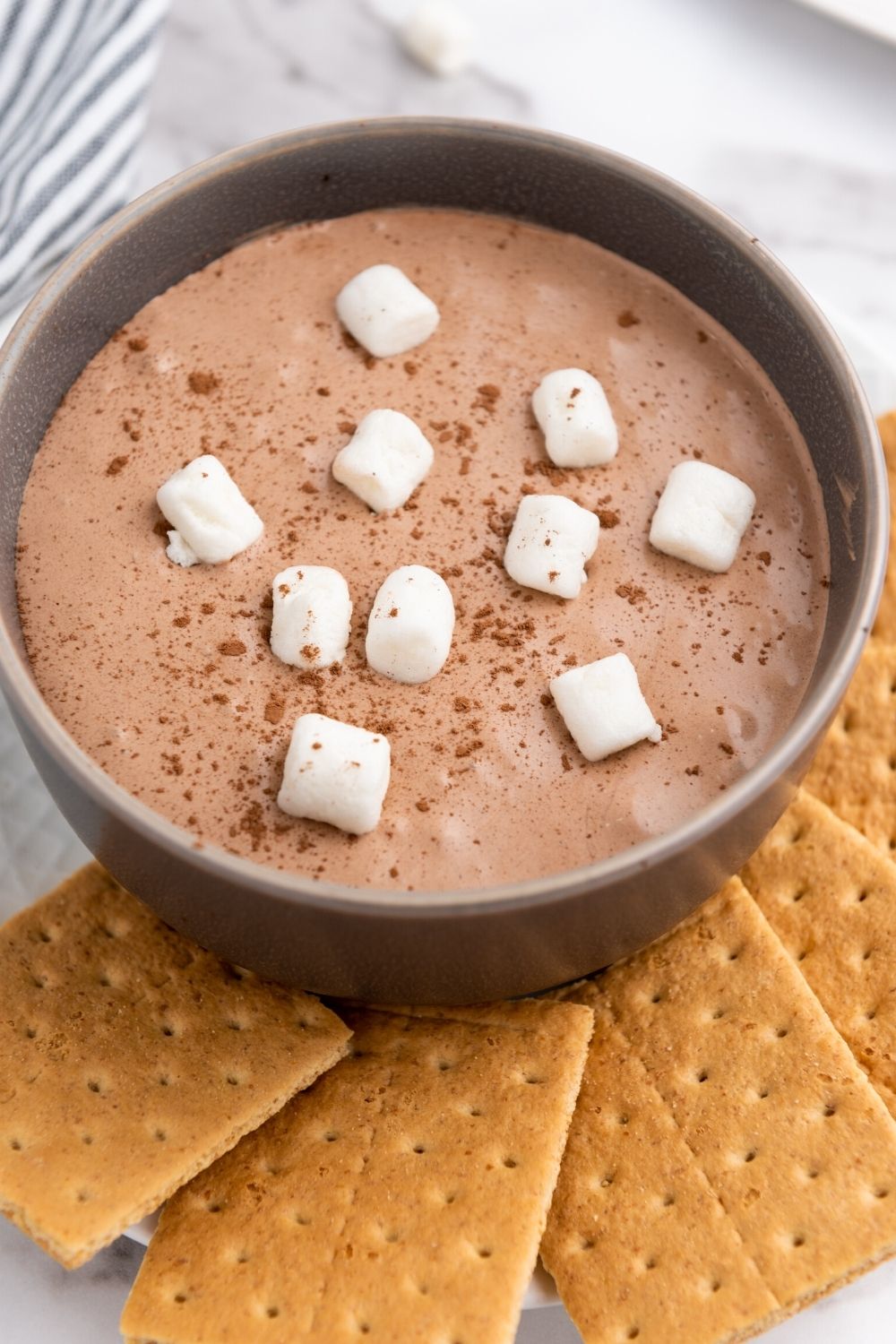 brown bowl of hot chocolate dip topped with marshmallows, served with graham cracker squares