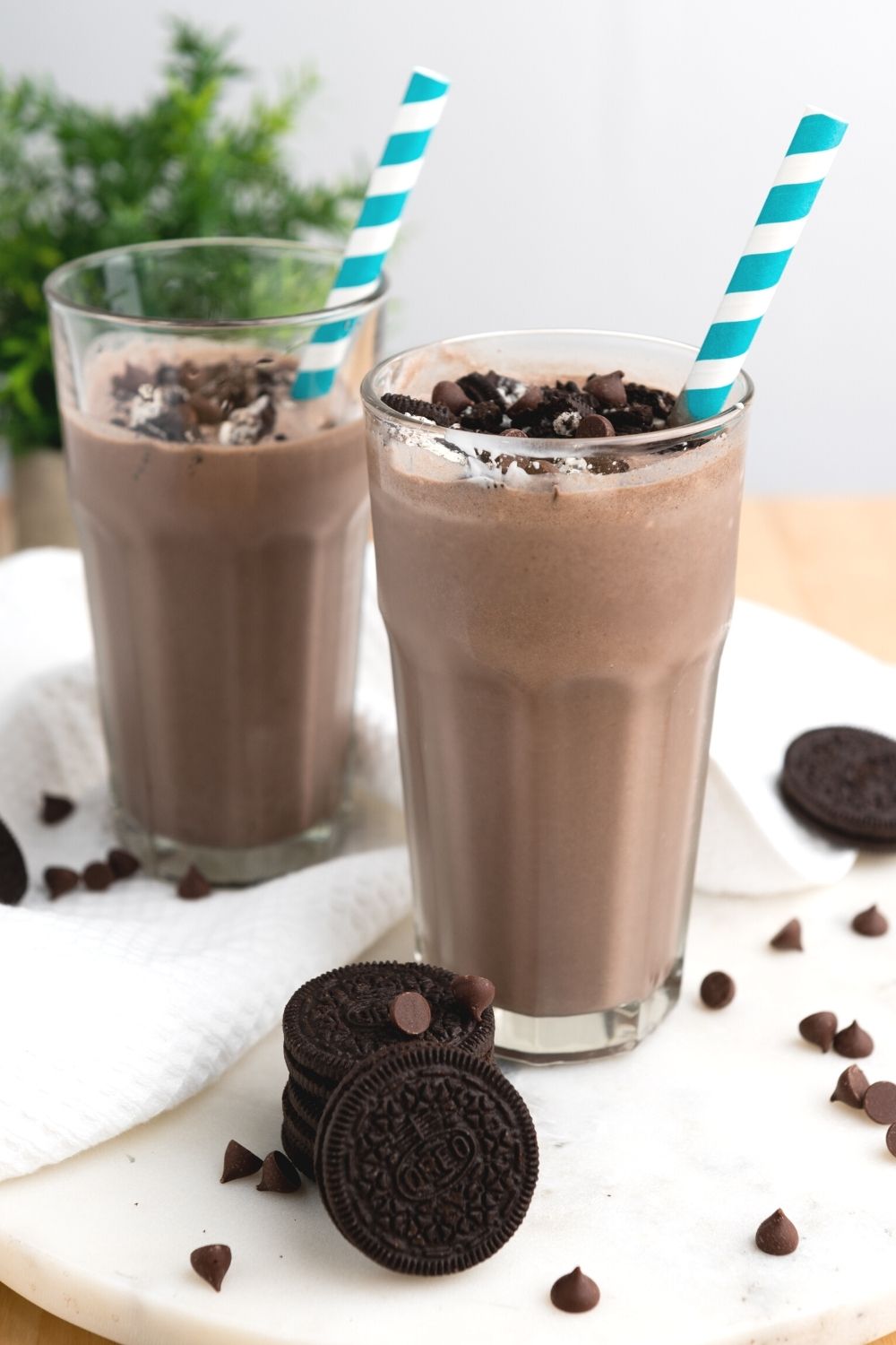 two glasses of Oreo milkshakes made without ice cream, with chocolate chips and Oreo cookies scattered around the glasses