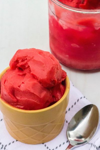 a serving of ninja creami cherry pie sorbet sits in front of the remaining pint of sorbet