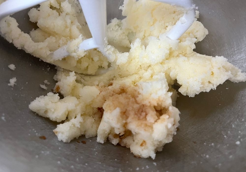 vanilla and almond extracts added to butter and sugar mixture in the bowl of a stand mixer