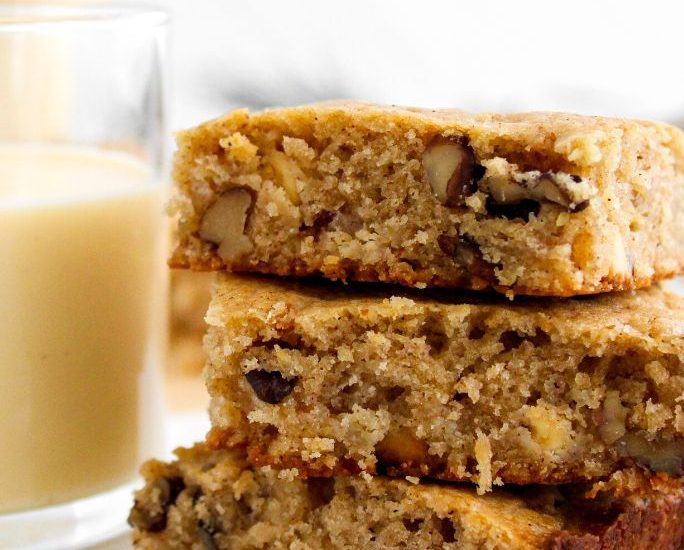 three eggnog blondies stacked together, with a glass of eggnog off to the side