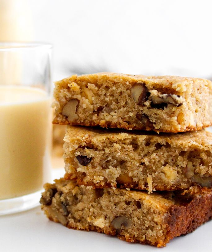 three eggnog blondies stacked together, with a glass of eggnog off to the side
