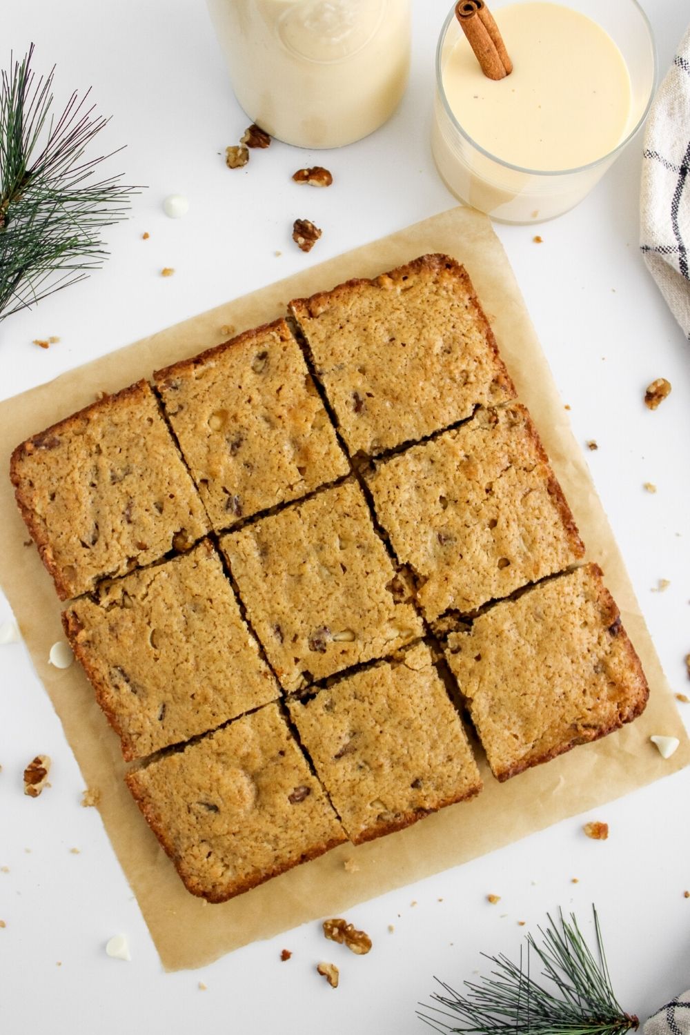 sliced eggnog blondies on parchment paper, with a glass of eggnog in the background