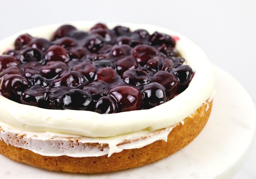 white cake layer with a border of frosting around the edge, filled with cherry filling