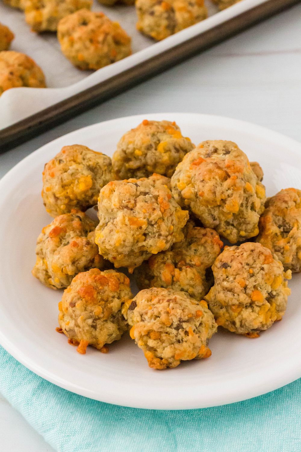 sausage balls served on a white plate, with a baking sheet of sausage balls in the background