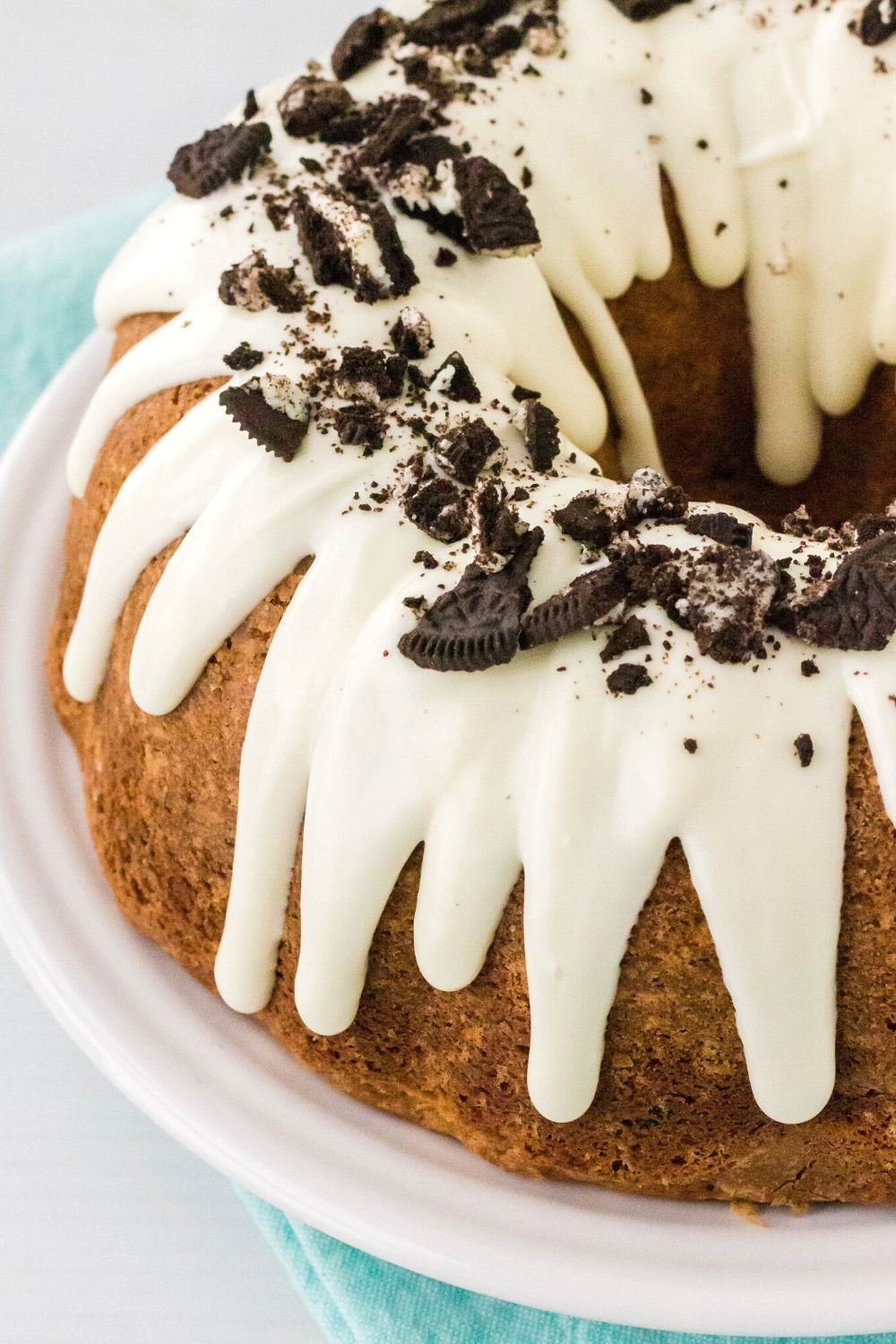 angled view of a whole cookies and cream pound cake, topped with cream cheese drizzled icing and crushed Oreo cookies