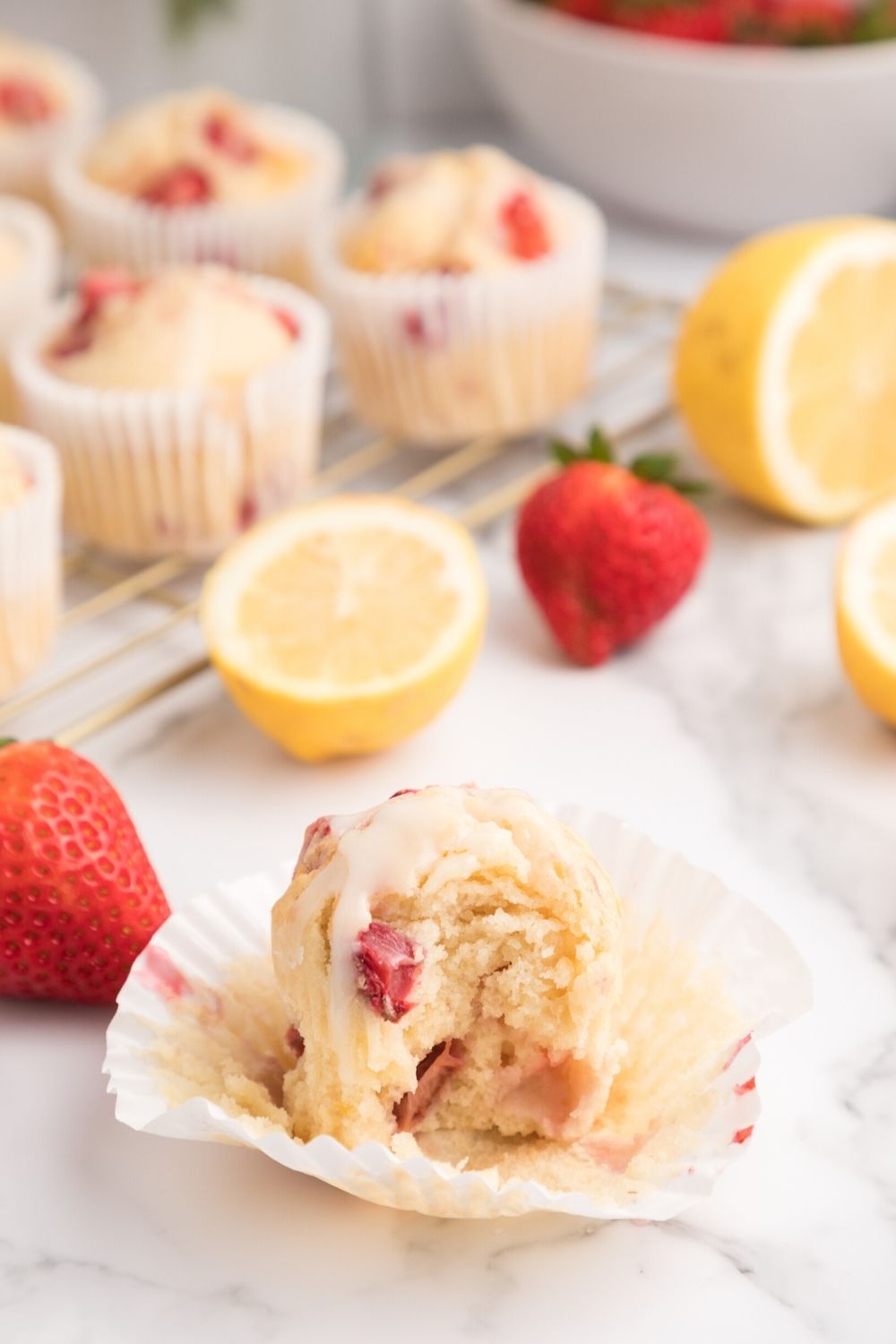 unwrapped strawberry lemon muffin, with frosting on top, in front of other muffins