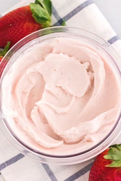 overhead view of a pint of ninja creami strawberry ice cream, with fresh strawberries scattered around the pint.
