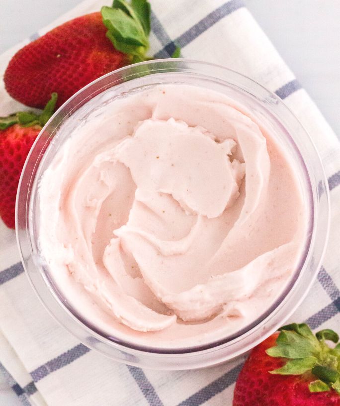 overhead view of a pint of strawberry ninja creami ice cream, with fresh strawberries scattered around the pint.