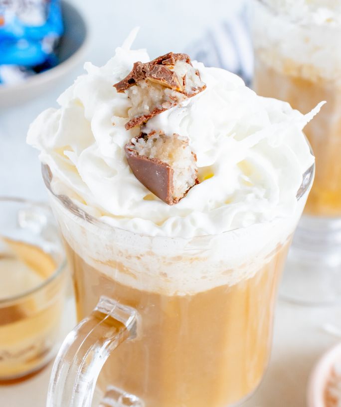 almond joy latte in a glass mug, topped with whipped cream and chopped almond joy candy bars