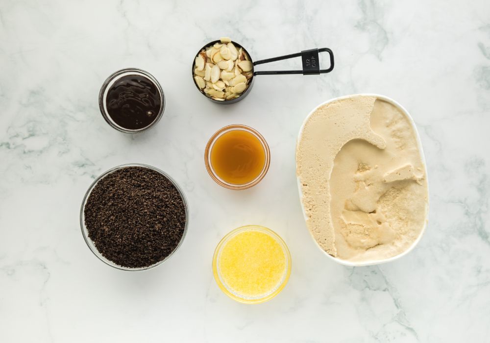 Laying out the ingredients needed to make a copy of the Billy Miner pie, including Oreo cookie crumbs, butter, mocha ice cream, sliced ​​almonds, caramel sauce, and chocolate sauce.
