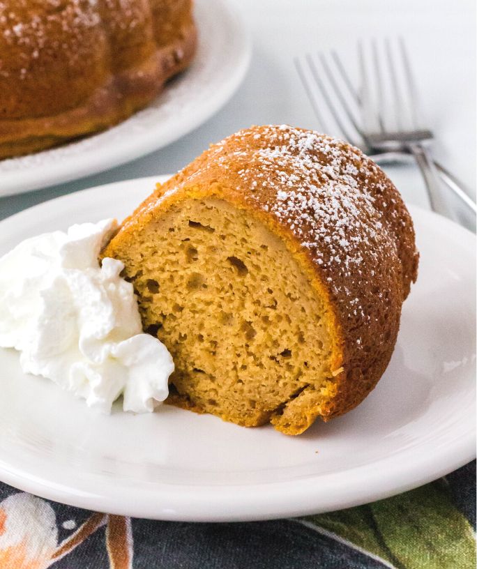 a slice of sweet potato bundt cake from a mix is served on a white plate, alongside some whipped cream