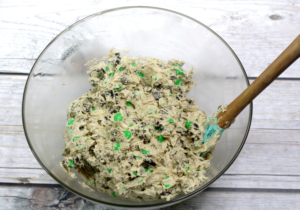 overhead view of a mixing bowl with M&Ms and Oreo pieces mixed into cookie dough.
