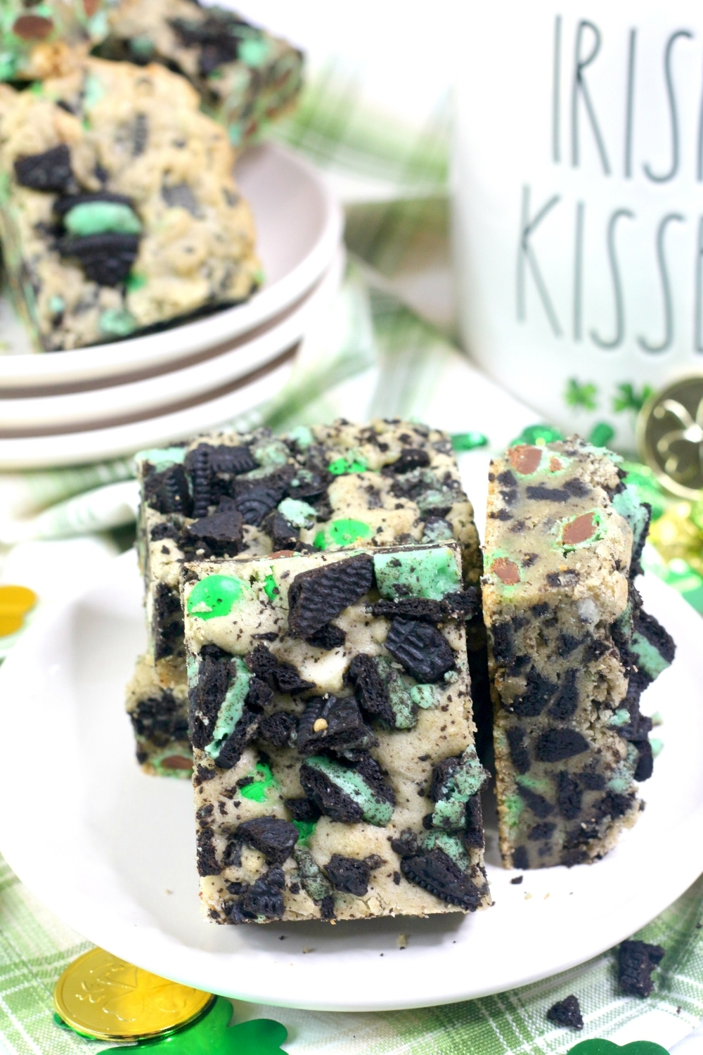 a white plate with a few mint Oreo cookie bars on it, with more cookie bars in the background, along with miscellaneous St. Patrick's Day decorations.